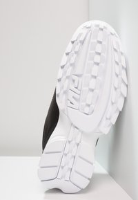 Sohle eines schwarz-weißen FILA Sneakers, die ein texturiertes Profilmuster und das erhabene FILA-Logo zeigt, auf einer weißen Oberfläche liegend.