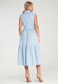 Jasnoniebieska sukienka bez rękawów z kołnierzykiem, dopasowanym wcięciem w talii i warstwową spódnicą. Materiał wydaje się gładki z lekką teksturą.