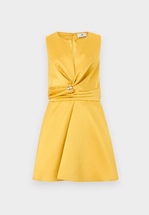 Κίτρινο φόρεμα από σατέν χωρίς μανίκια, με στρίφωμα μπροστά συγκεντρωμένο σε χρυσό δαχτυλίδι στη μέση και φαρδιά φούστα.