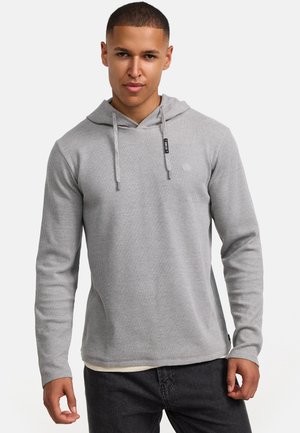 Sudadera gris con canalé, bolsillo tipo canguro y cordones ajustables. Mangas largas y un corte relajado, superpuesta a una camiseta de color claro.