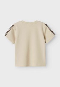 Camiseta de manga corta color crema con textura acanalada, escote redondeado y una franja marrón en cada manga con acentos de texto en blanco.