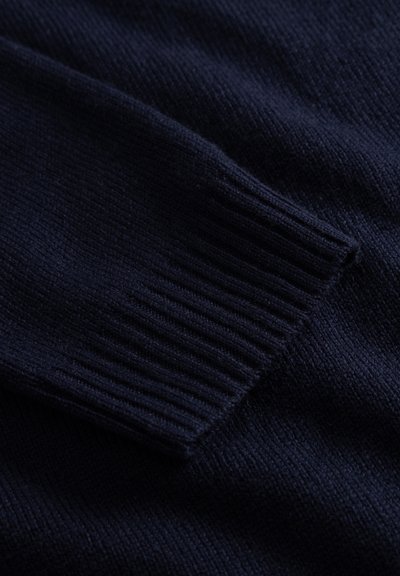 Navy blue knitted sweater fabric featuring a ribbed cuff and smooth texture, with a subtle sheen and consistent stitching pattern.
