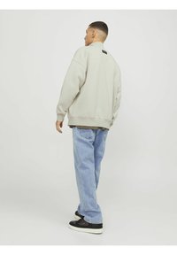 Lysegrå oversized sweatshirt med høj hals og ribbede manchetter, parret med lyseblå jeans og sorte sneakers. Bagperspektiv.