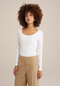 Top blanco de manga larga con canalé y escote redondeado, combinado con pantalones beige de cintura alta, ajustados. Textura de algodón suave.