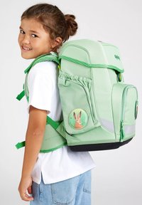 Mochila verde claro con correas acolchadas, bolsillos frontales y una insignia de conejo. Incluye acentos reflectantes y un acabado texturizado.