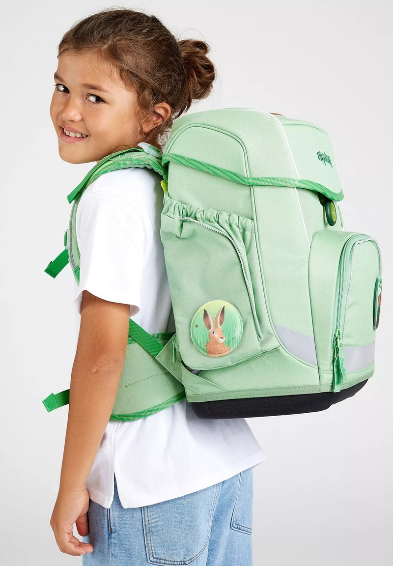 Mochila verde claro con correas acolchadas, bolsillos frontales y una insignia de conejo. Incluye acentos reflectantes y un acabado texturizado.