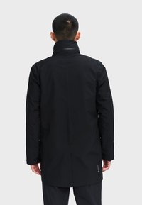 Giacca impermeabile nera con colletto alto, maniche lunghe e vestibilità dritta. Caratteristiche includono il marchio Gore-Tex sull'orlo e dettagli di cucitura minimi.