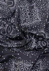 Μαύρο ύφασμα με λευκά πουά μοτίβα που σχηματίζουν αφηρημένα κυκλικά και αστεροειδή σχήματα, παρουσιάζοντας πτυχώσεις και ομαλή υφή.