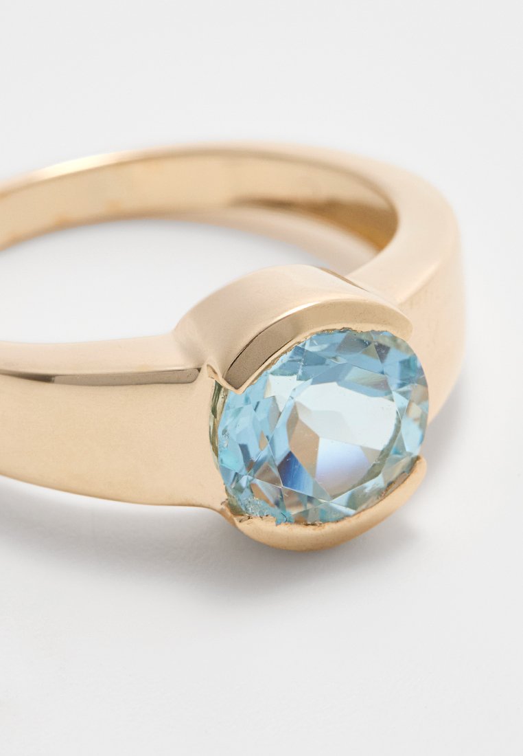 Goldfarbener Metallring mit einem großen, facettierten, hellblauen Edelstein mit glatten, runden Kanten und einer polierten Oberfläche.