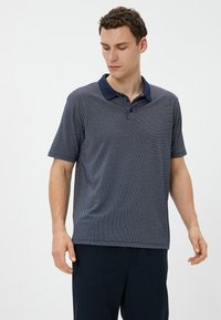 Camiseta polo de manga corta en azul marino con una textura estampada y un collar oscuro sólido; cierre de botones de tres; corte relajado.