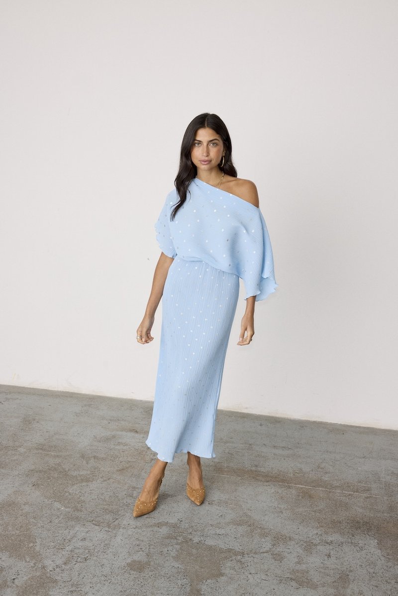 Robe tricotée bleu clair avec encolure asymétrique, corsage texturé et rayures verticales. De petits points blancs ajoutent un motif. Talons aiguilles tannés.