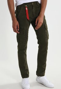 Pantalones cargo verde oliva con múltiples bolsillos, hechos de un tejido duradero, con cierre de cremallera y una etiqueta roja unida a la cinturilla.