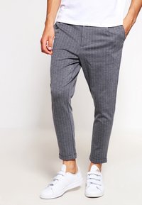 Grijze gestreepte broek van lichtgewicht stof, met een tapered fit en opgerolde zomen, gecombineerd met witte sneakers.