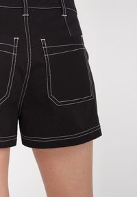 Zwarte denimshorts met witte stiksels, voorzien van twee achterzakken en een recht gesneden zoom. De stof vertoont een lichte textuur.
