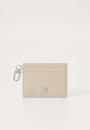 Beige leather cardholder with four slots, featuring a small silver hardware logo and a keyring attachment. Smooth texture, minimal design.