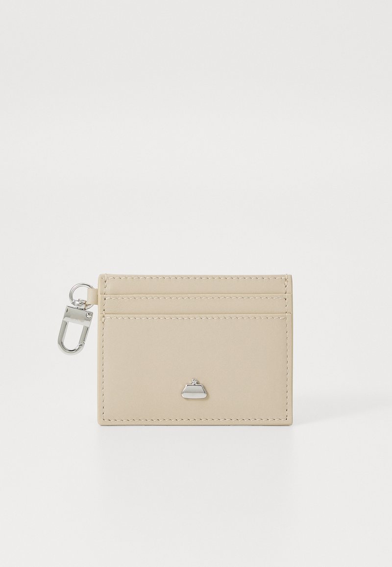 Beige leather cardholder with four slots, featuring a small silver hardware logo and a keyring attachment. Smooth texture, minimal design.