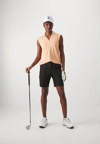 Golfantrekk med ferskenfarget ermeløs poloskjorte og svarte shorts. Inkluderer en hvit cap og golfkølle. Skoene er hvite og teksturerte.