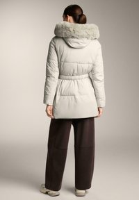 Parka c�ăptușită de culoare gri deschis, cu guler din blană ecologică, talie strânsă și material moale. Prezintă mâneci lungi și o croială lejeră, având o lungime până la mijlocul coapsei.