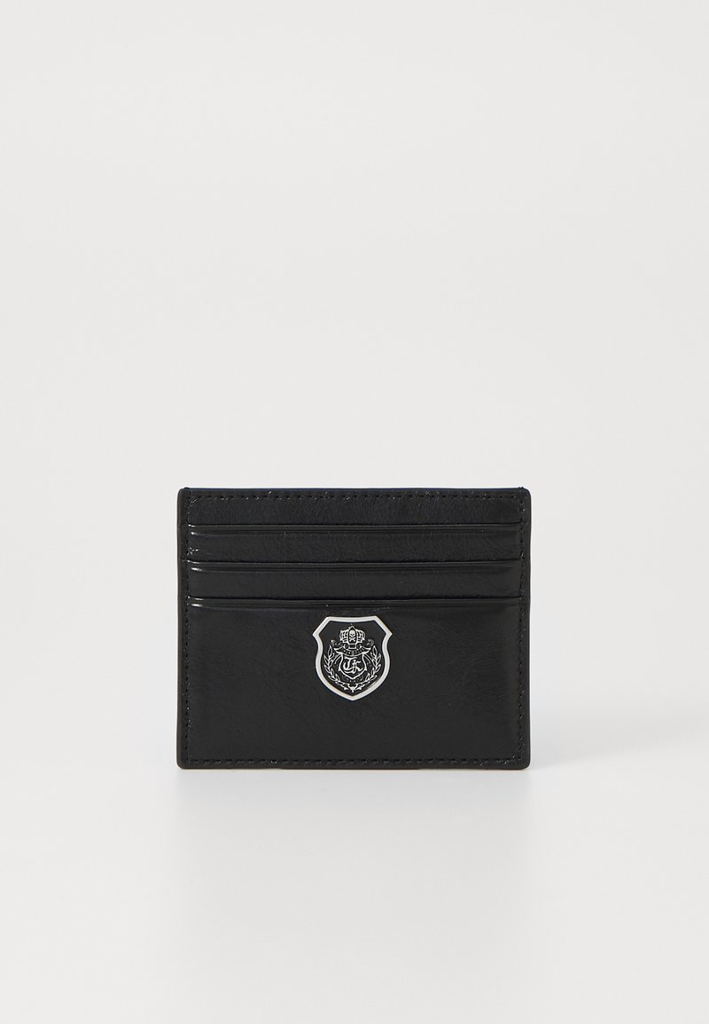 Porta-cartões em pele preta com quatro slots para cartões, uma superfície texturizada e um emblema prateado na parte frontal.