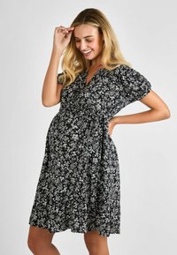 Abito nero floreale con maniche corte a sbuffo, scollo a V, vita arricciata e gonna fluente. Presenta motivi di fiori bianchi in tutto.