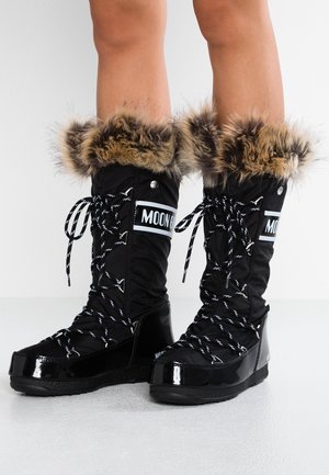 Bottes d'hiver noires avec bordure en fourrure, logo réfléchissant "MOON" et lacets épais à motifs, portées sur des jambes nues sur un fond uni.