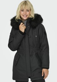 Svart polstret vinterjakke med faux pelskrage, elastisk midje, glidelås- og knappefester, samt sidelommer. Strukturert stoff og glatt overflate.