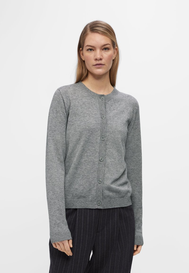 Grijze cardigan van zacht materiaal, met een ronde halslijn, lange mouwen en een knoopsluiting aan de voorkant. Getextureerde geribbelde manchetten.