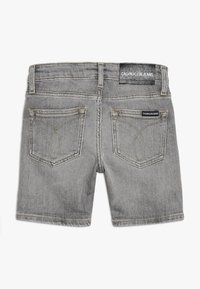 Harmaat farkkushortsit suoran leikkauksen kanssa, joissa on kaksi takataskua, näkyvät ompeleet ja Calvin Klein Jeans -logo vyötäröllä.