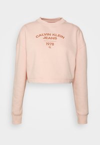 Sudadera corta de color rosa claro con un cuello alto, mangas largas y un gráfico frontal que presenta "CALVIN KLEIN JEANS 1978" en marrón.
