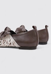 Ballerines en cuir marron avec un panneau en fourrure tacheté, un accent en nœud sur le bout, et une silhouette lisse et arrondie avec un petit talon.