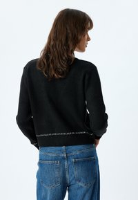 Svart stickad tröja med långa ärmar, ribbad nederkant och vit söm detalj längst ner; bärs med blå jeans.