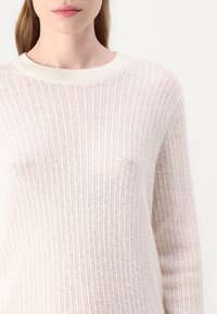 Lysbeige ribbet strikkegenser med rund hals og lange ermer, som har en myk tekstur og subtil dybde i fargen.