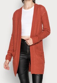 Cardigan lavorato a maglia color ruggine con apertura anteriore, bordi a coste e due tasche anteriori. Presenta un motivo testurizzato e maniche lunghe.