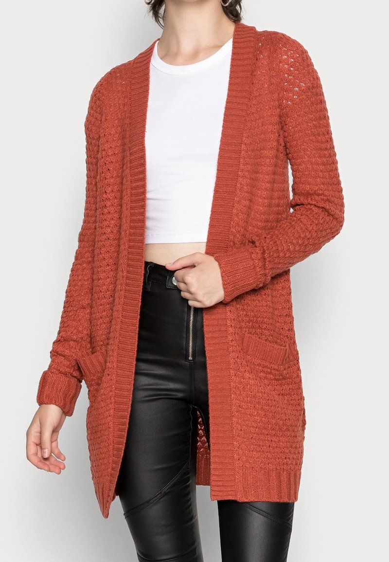 Cardigan lavorato a maglia color ruggine con apertura anteriore, bordi a coste e due tasche anteriori. Presenta un motivo testurizzato e maniche lunghe.