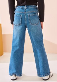 Jean large en denim bleu avec taille haute, présentant des poches arrière et un ourlet brut. Le tissu a une texture classique et un délavage moyen.