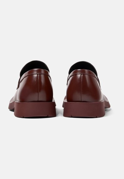 Scarpe slip-on in pelle marrone con punta arrotondata, dettagli di cucitura sottili e suola piatta in gomma, viste dal retro.