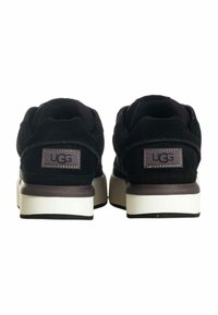 Le sneakers in suede nero presentano una suola platform bianca a contrasto. Sul retro è presente un'etichetta marrone con il logo UGG. Design semplice con forma arrotondata.