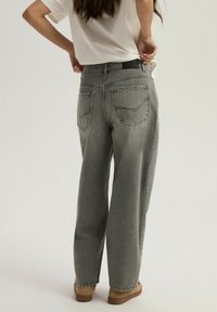 Szare dżinsy z szerokimi nogawkami o wyblakłej fakturze, z dwiema tylnymi kieszeniami i podkreślonymi szwami. Połączone z białą bluzką i brązowym obuwiem.