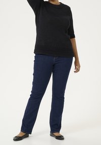 Czarny sweter z teksturowanego dzianiny, z rękawami do połowy łokcia, w połączeniu z ciemnoniebieskimi jeansami o prostych nogawkach i czarnymi skórzanymi balerinami.