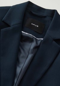Blazer navy avec col à revers. Doublure intérieure en satin lisse, avec étiquette OPUS. Matière texturée, design structuré.