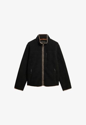 Chaleco de forro polar negro con cuello alto, cremallera frontal completa y dos bolsillos con cremallera. Ribete beig a lo largo de la cremallera y el dobladillo.