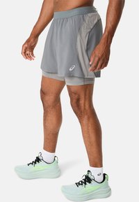 Grå atletiske shorts med en kontrasterende lysere grå sidelogo, udstyret med en flad talje og et logo på fronten. Løbesko i akryl i mintgrøn.