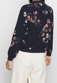 Marineblauwe sweatshirts met roze en grijze bloempatronen, ribgebreide manchetten en onderkant. Zacht stof en een relaxte pasvorm, gedragen met lichtgekleurde broeken.