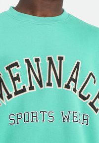 Felpa verde realizzata in tessuto misto cotone, con testo nero e beige "MENACE SPORTS WEAR" in lettering curvo sul petto.