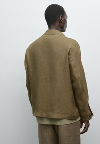 Brown linen jacket with a relaxed fit, single-button cuff, and a classic collar. The texture is soft, with a subtle weave pattern.