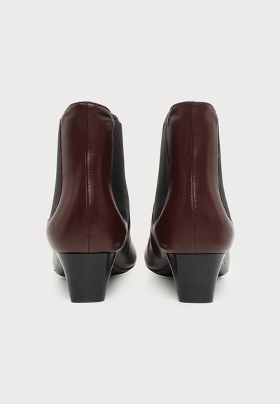 Paire de bottines en cuir marron foncé avec panneaux latéraux élastiques noirs et petits talons carrés, vues de dos sur fond blanc.