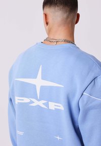 Lichtblauwe sweatshirt van zacht materiaal met een grote witte grafische print van "PXP" en sterontwerpen op de achterkant, met ribbelmanchetten.