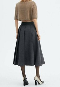 Maglione corto marrone a maglia con maniche corte abbinato a una gonna midi plissettata grigia. Tacchi bicolore neri e crema completano l'outfit.