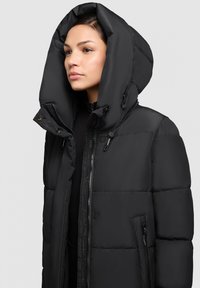 Czarna kurtka puchowa z dużym kapturem, wyposażona w zamek błyskawiczny z przodu, kieszenie boczne oraz pikowany wzór dla lepszej izolacji. Gładka faktura.
