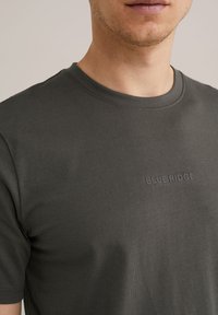 Mörkgrå t-shirt med kort ärm av bomull och rund hals; har en präglad "BLUE RIDGE"-logotyp på bröstet. Slät textur.